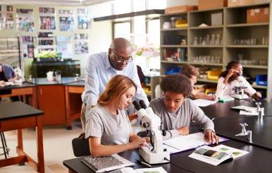 High School 学生 With Tutor Using Microscope In Biology 